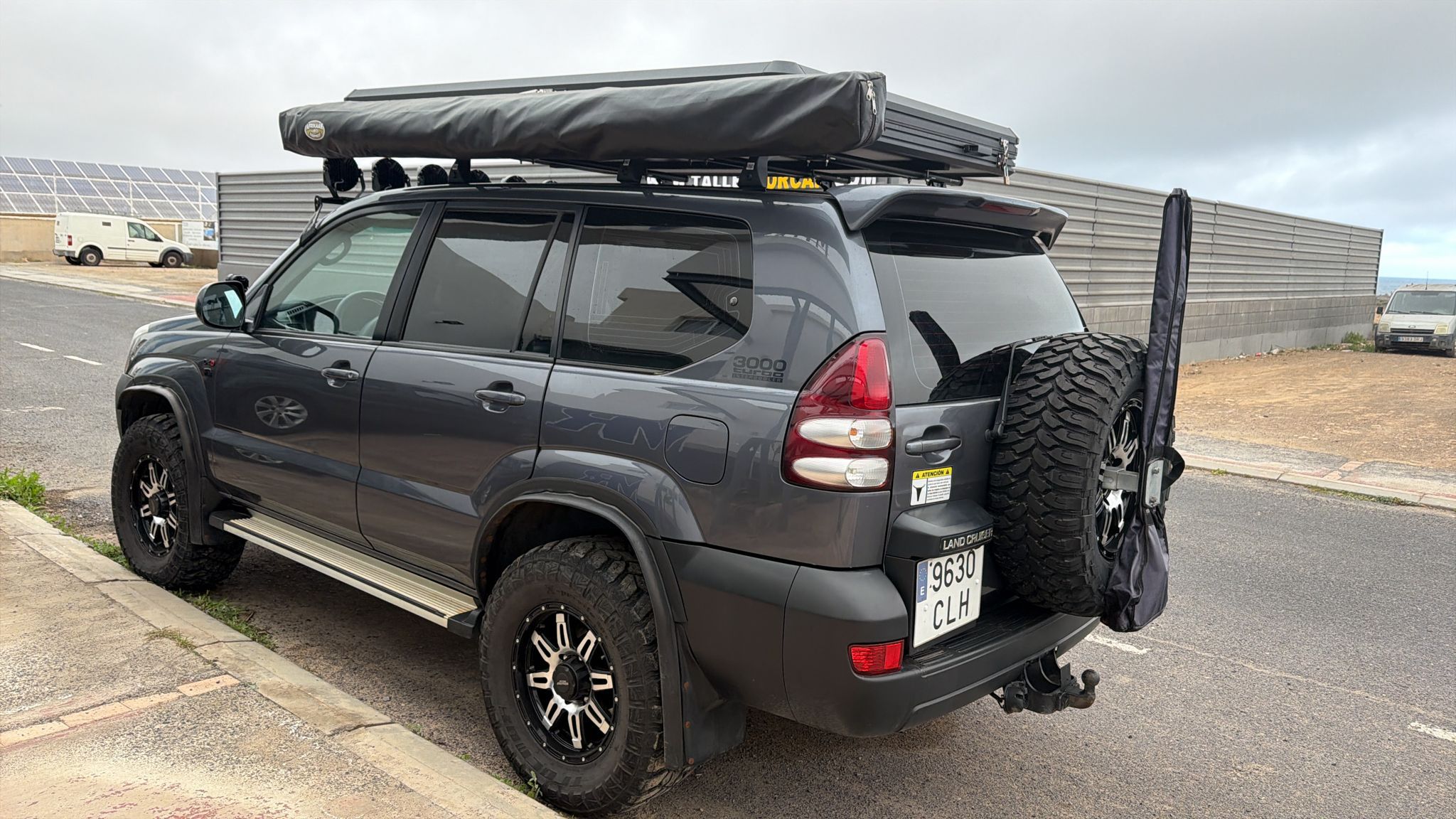 SUV Toyota Land Cruiser con toldo en el techo, llantas de gran tamaño y estribos laterales, aparcada en una calle.