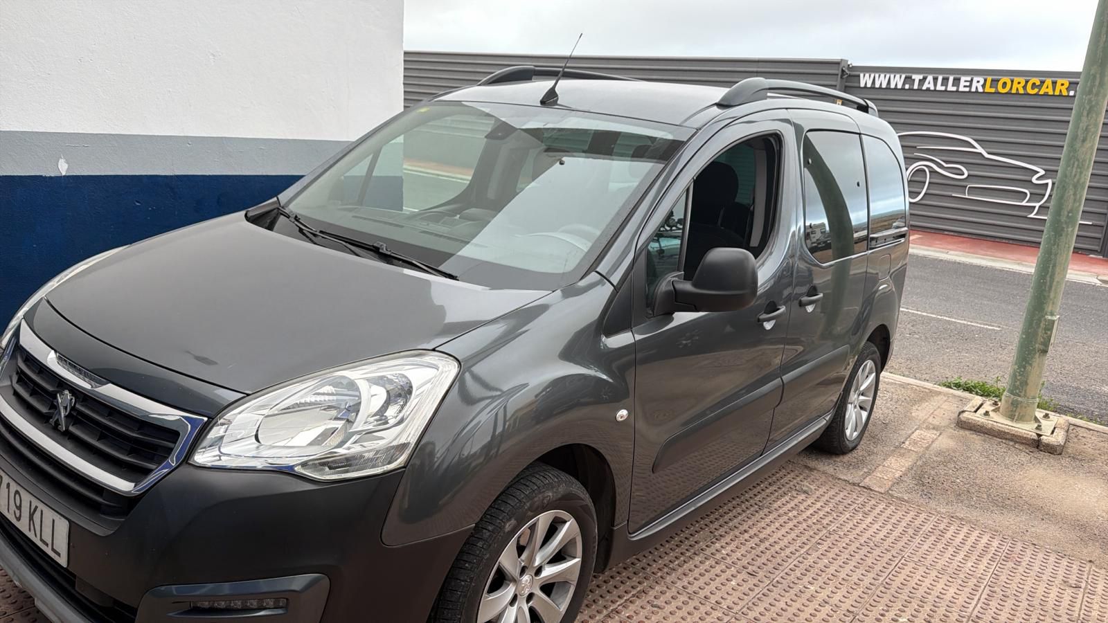 Furgoneta Peugeot gris estacionada frente a un taller mecánico, mostrando su diseño moderno y funcional.