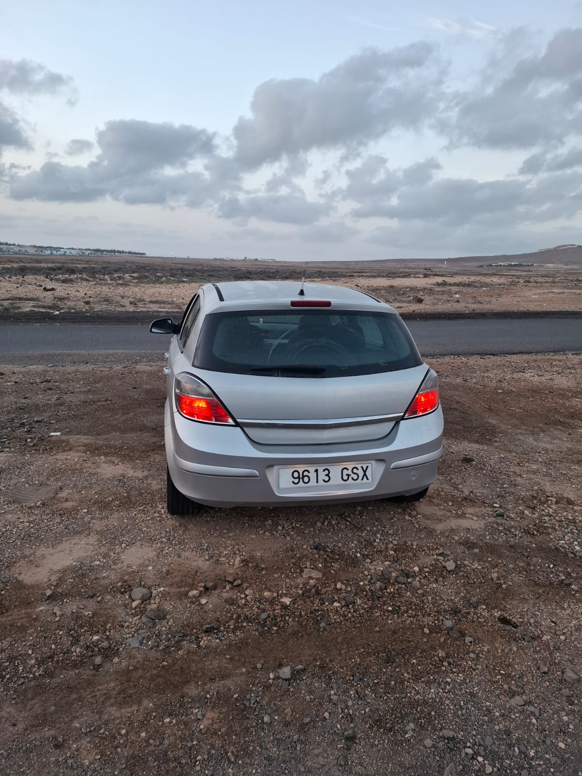 Automóvil plateado estacionado en un terreno árido, con un paisaje desértico y cielo nublado al fondo.