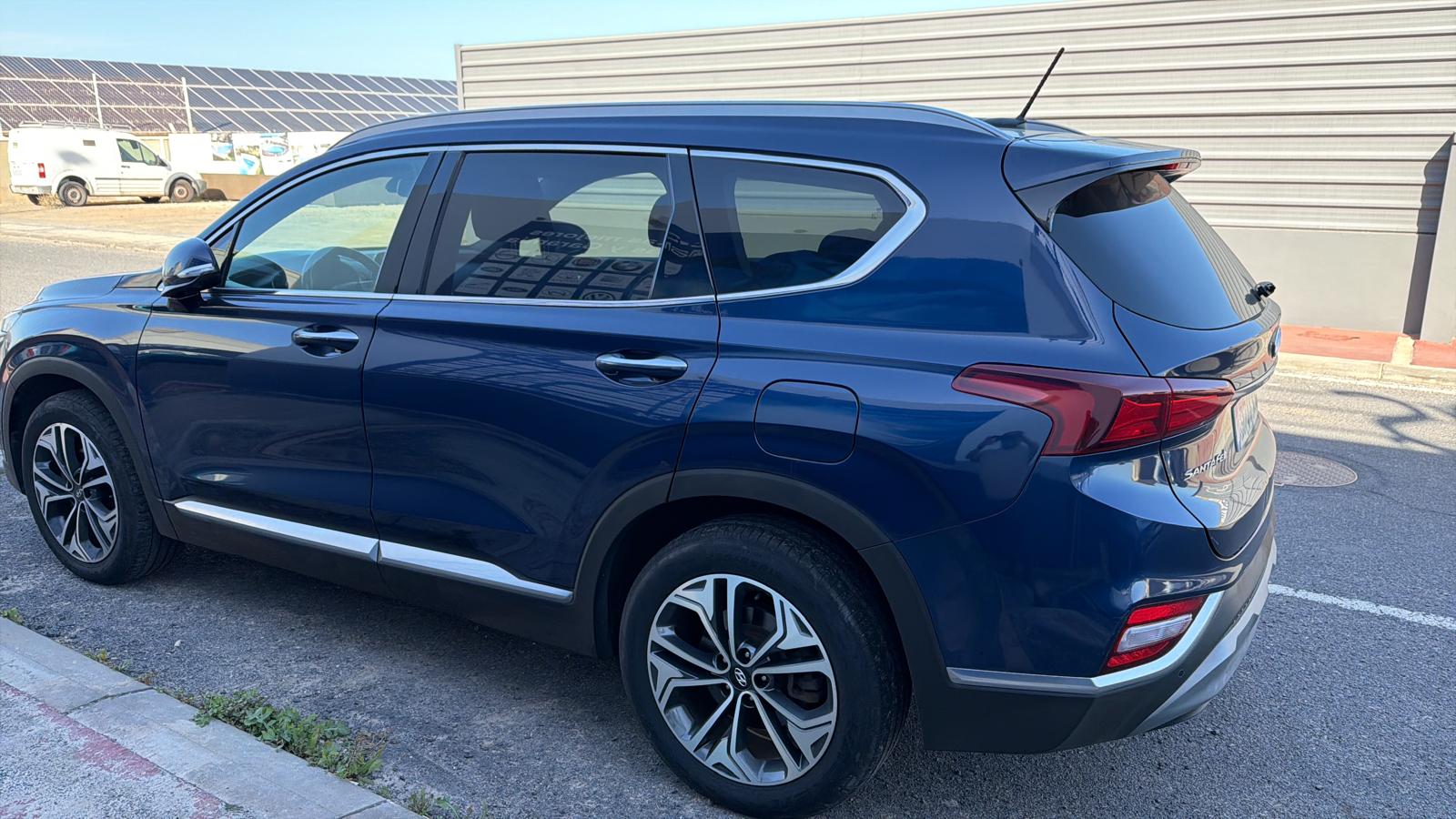 SUV azul estacionado en la calle, con llantas de diseño moderno y detalles metálicos en el borde. Fondo con paneles solares y vehículos estacionados.