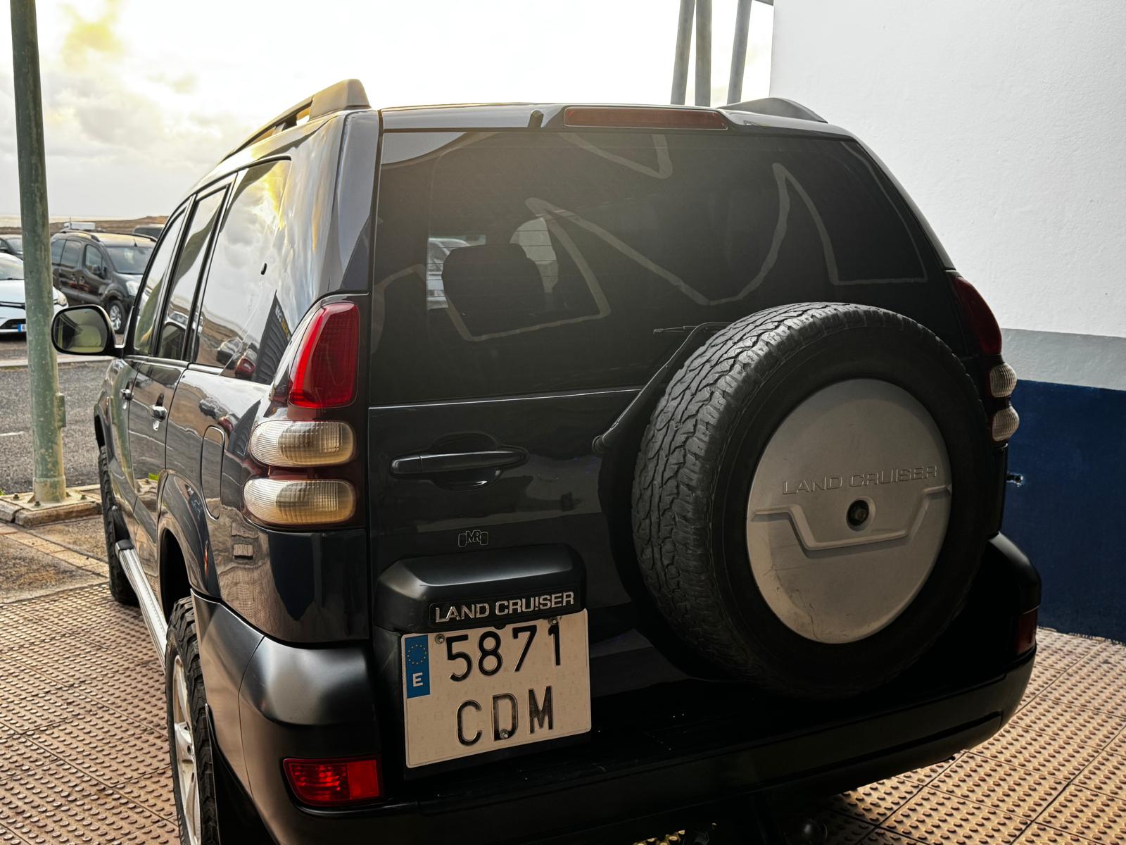 SUV Toyota Land Cruiser negra estacionada, vista trasera con llanta de repuesto, matrícula E 5871 CDM, en un entorno urbano.