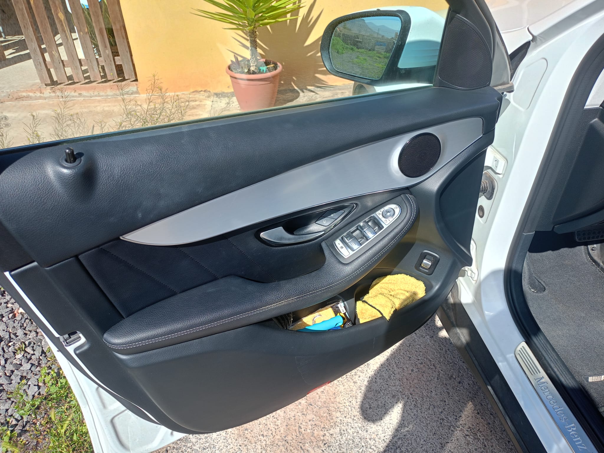 Detalle del interior de la puerta del lado del conductor de un automóvil Mercedes-Benz, mostrando el panel de control de ventanas, altavoces y un paño amarillo en el compartimento inferior.