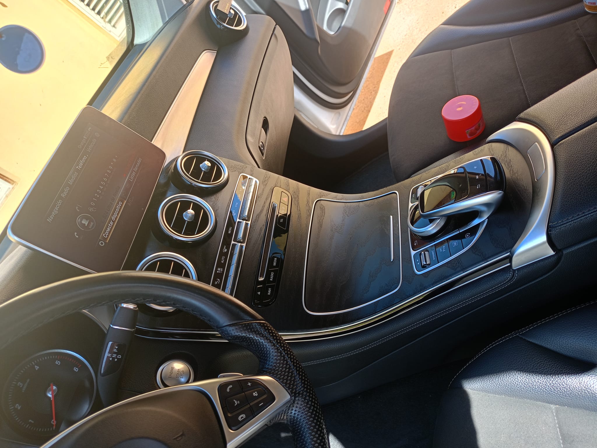 Interior de un automóvil de lujo, mostrando el panel central con pantalla digital, controles de climatización y sistema de audio, volante deportivo y detalles en cuero negro.