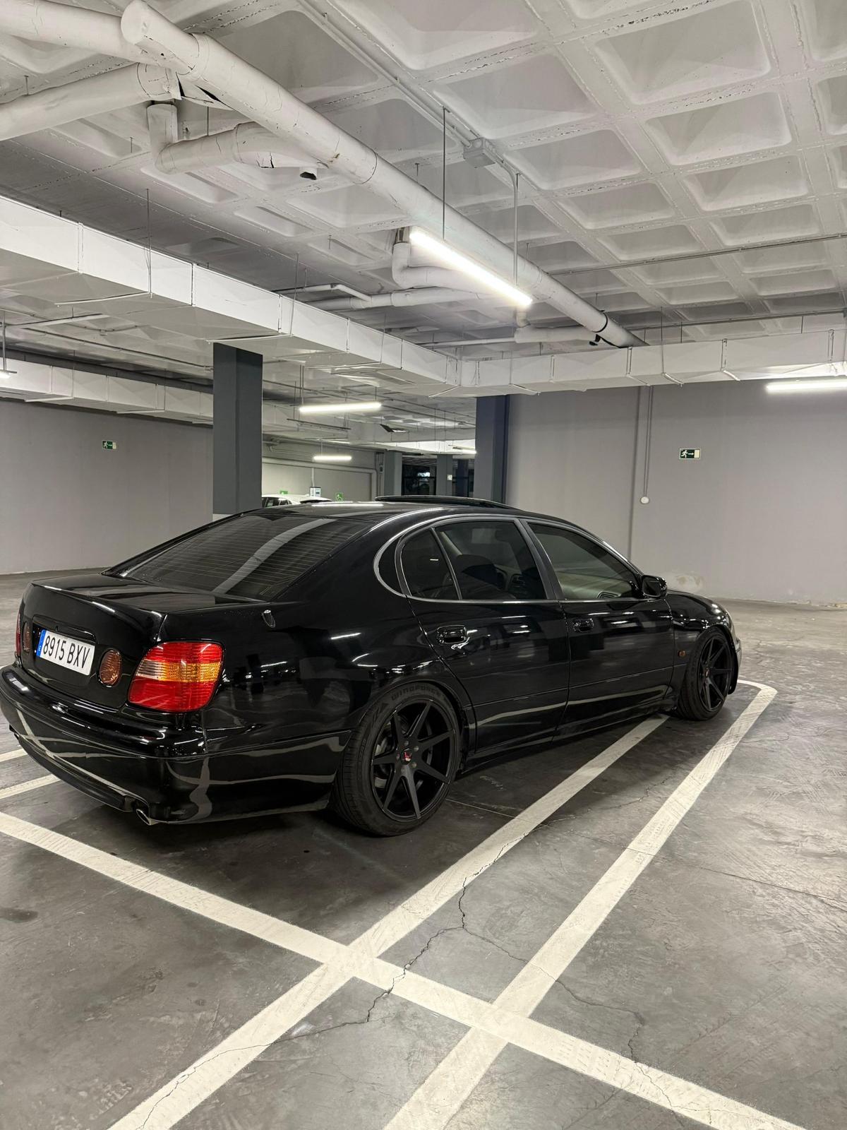 Auto negro estacionado en un garaje, con llantas de aleación y un diseño elegante. El fondo muestra una estructura moderna y bien iluminada.