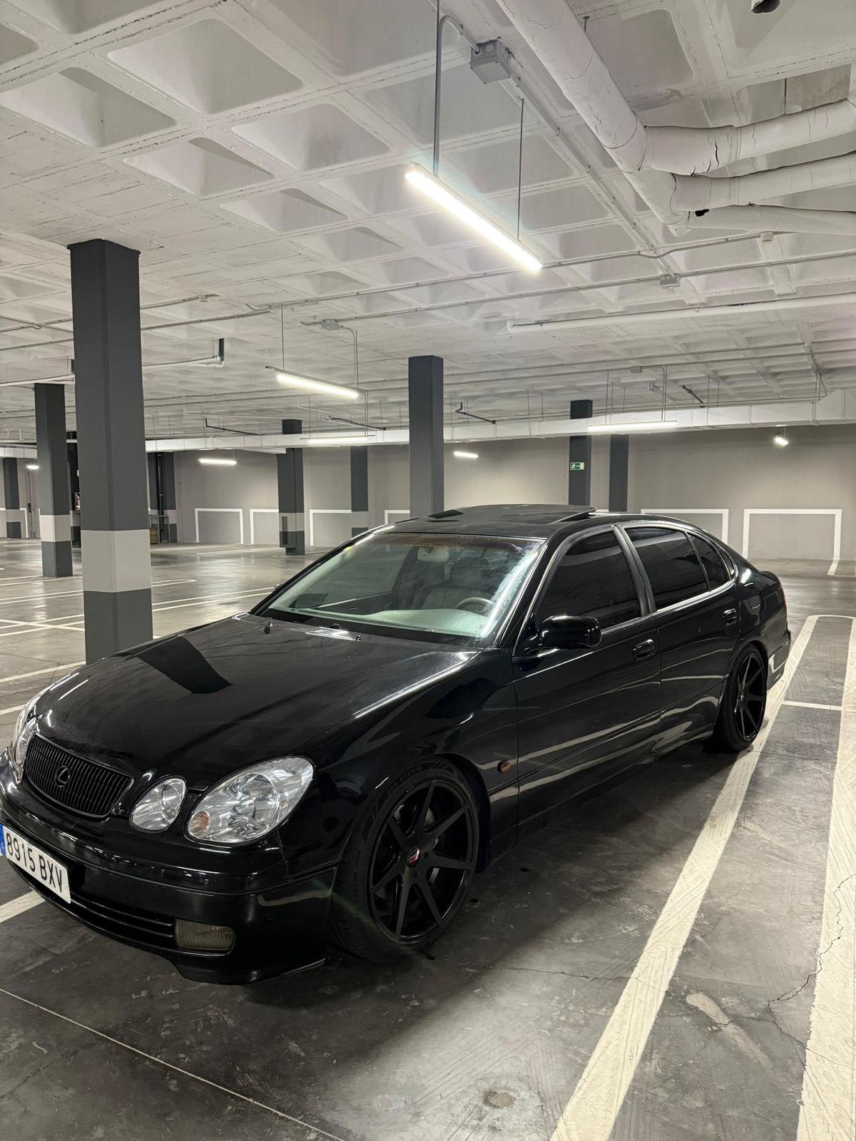 Coche Lexus negro estacionado en un aparcamiento subterráneo, con llantas negras y un diseño elegante. Iluminación moderna y ambiente urbano.