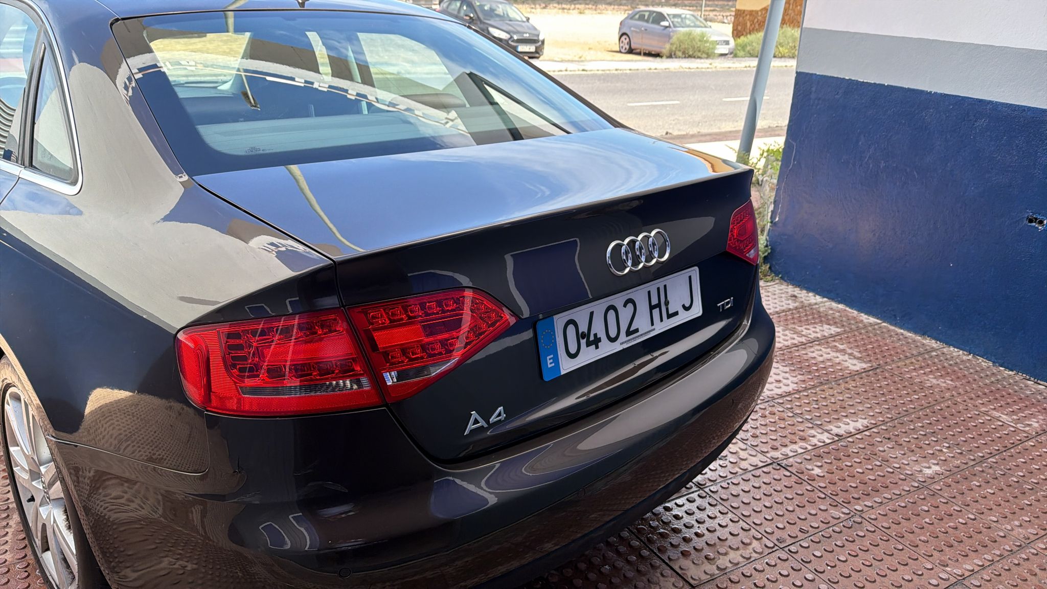 Audi A4 negro estacionado, mostrando la parte trasera y el diseño de los faros. Se observa la matrícula con el código 0402 HLJ en un entorno urbano.