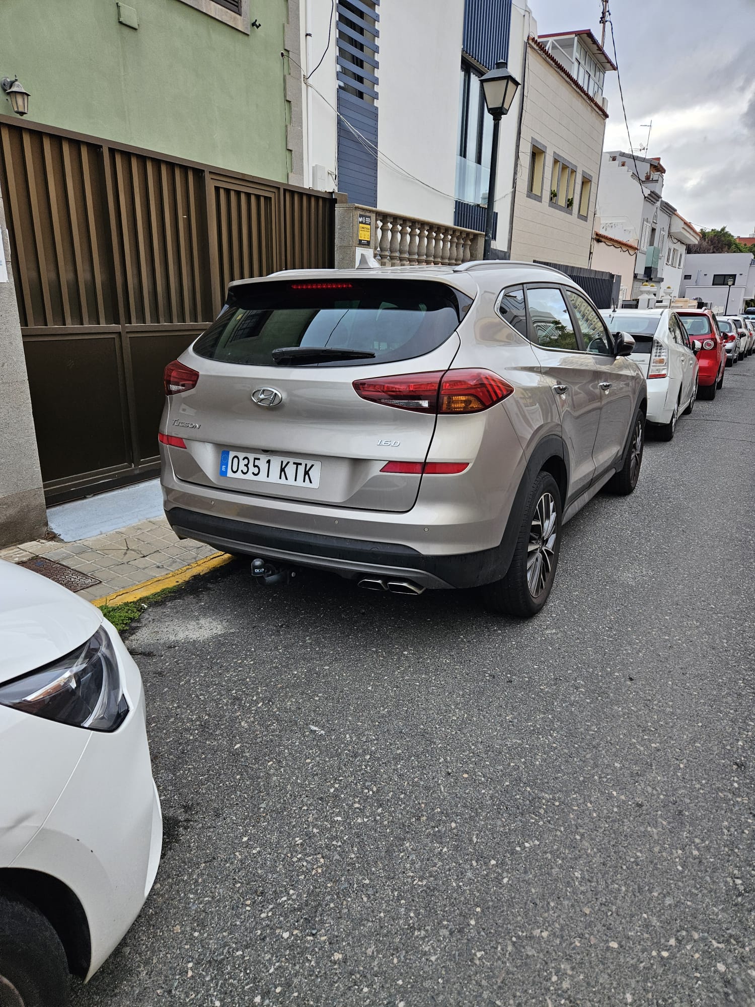 Vehículo Hyundai Tucson estacionado en una calle con edificios residenciales, mostrando su parte trasera y lateral. El coche es de color gris y tiene matrícula 0351 KTK.