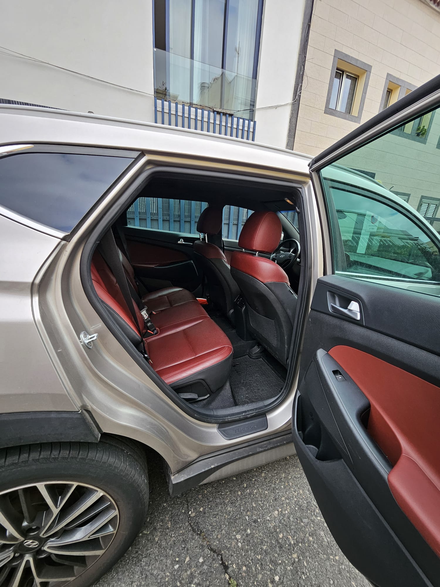 Interior de un coche con asientos rojos y puerta trasera abierta, mostrando el espacio disponible en la parte posterior. La imagen destaca el diseño moderno y cómodo del vehículo.