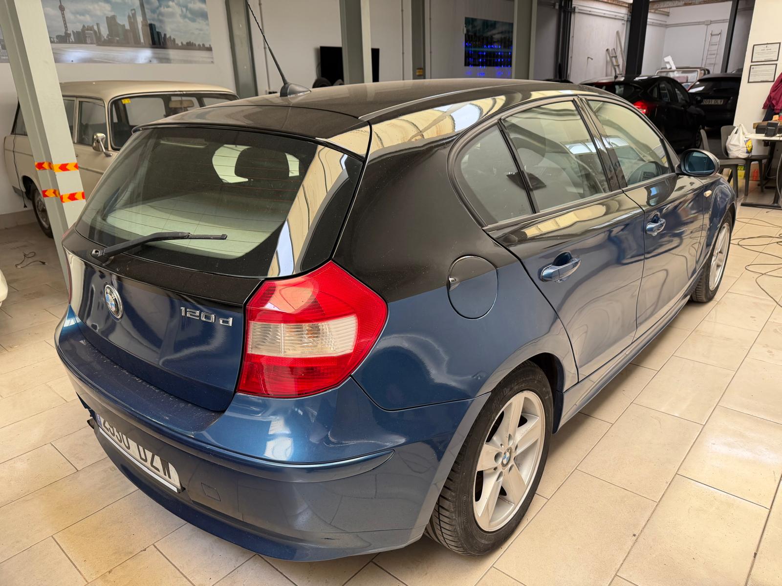 Imagen de un BMW 120d azul estacionado en un taller, mostrando su diseño hatchback y detalles como el techo negro y llantas de aleación.