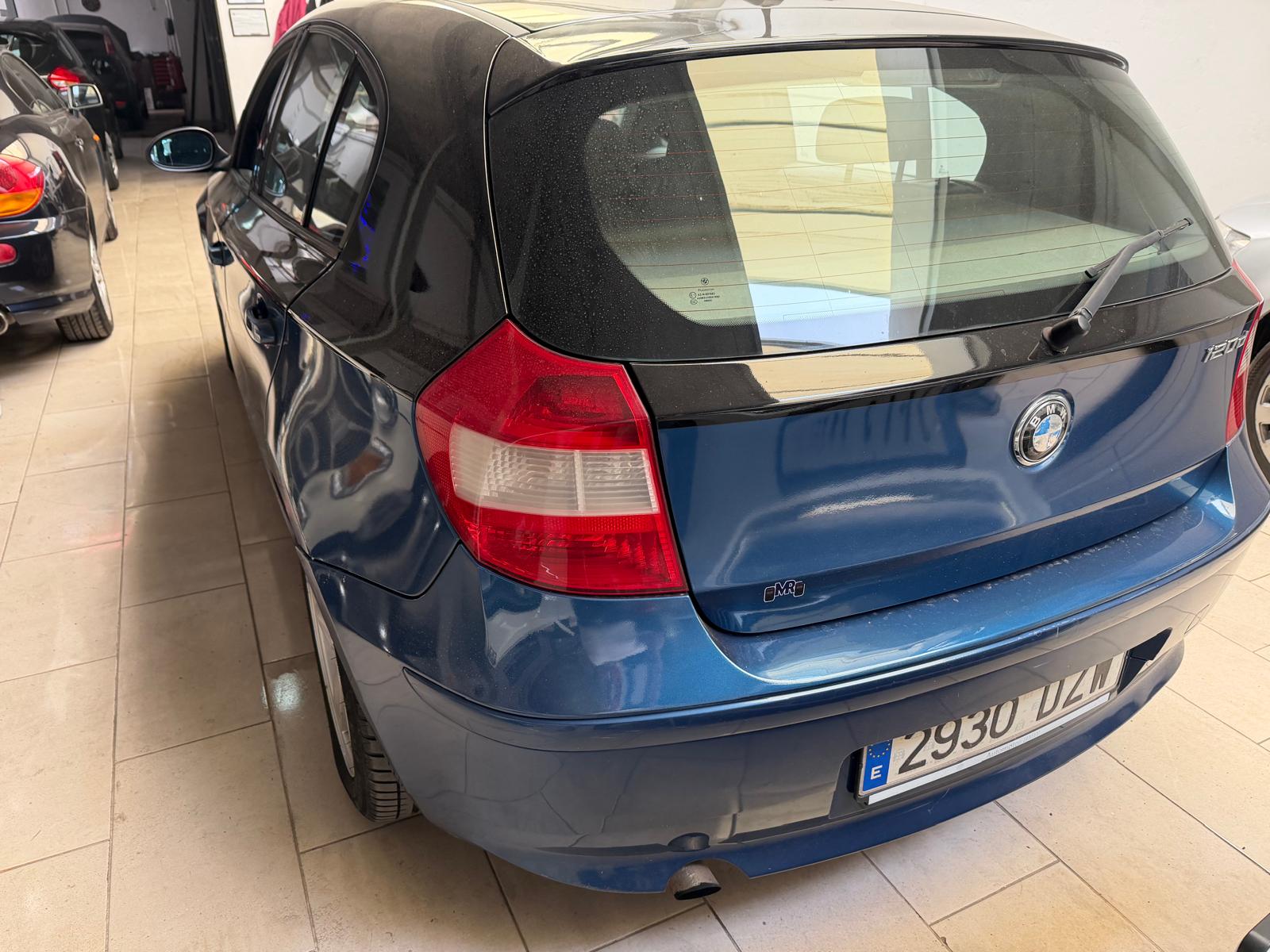 Auto BMW 120d de color azul estacionado en un garaje, mostrando la parte trasera y detalles del diseño.