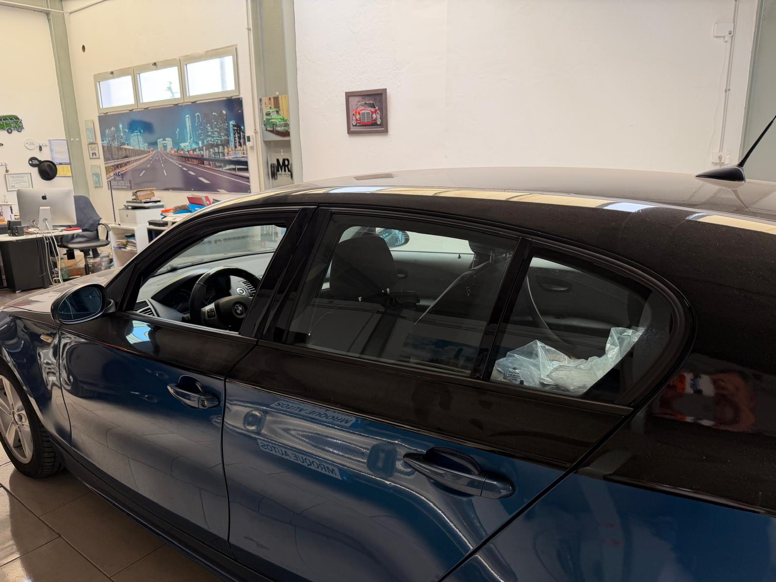 Automóvil azul estacionado en un taller con un diseño moderno, mostrando el interior y el volante visible. Al fondo, se aprecian elementos de oficina y decoración relacionada con automóviles.