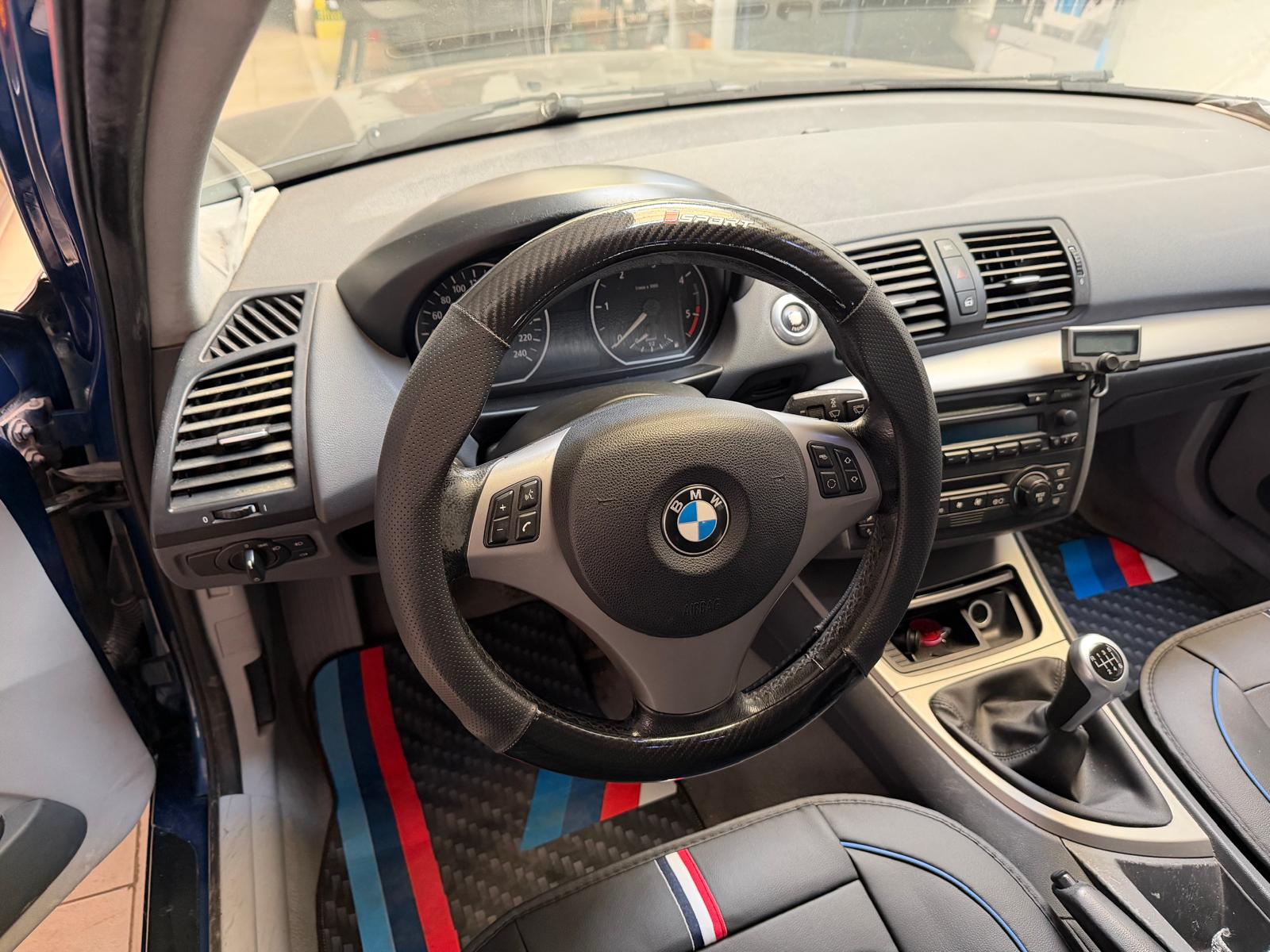 Interior de un automóvil BMW, mostrando el volante, el tablero de instrumentos y la consola central con detalles en fibra de carbono y asientos con tapicería deportiva.