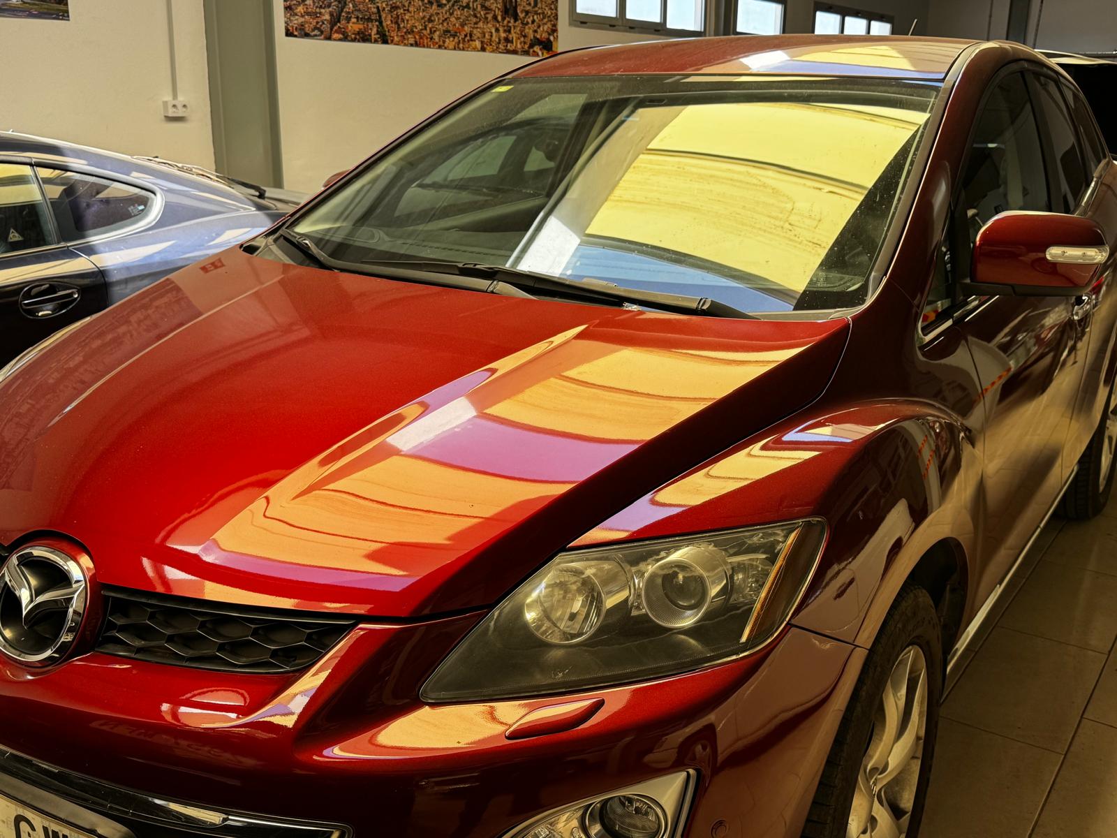 Mazda CX-7 roja estacionada en un garaje, destacando su diseño elegante y pulido. El vehículo presenta un acabado brillante y detalles en la parrilla frontal.
