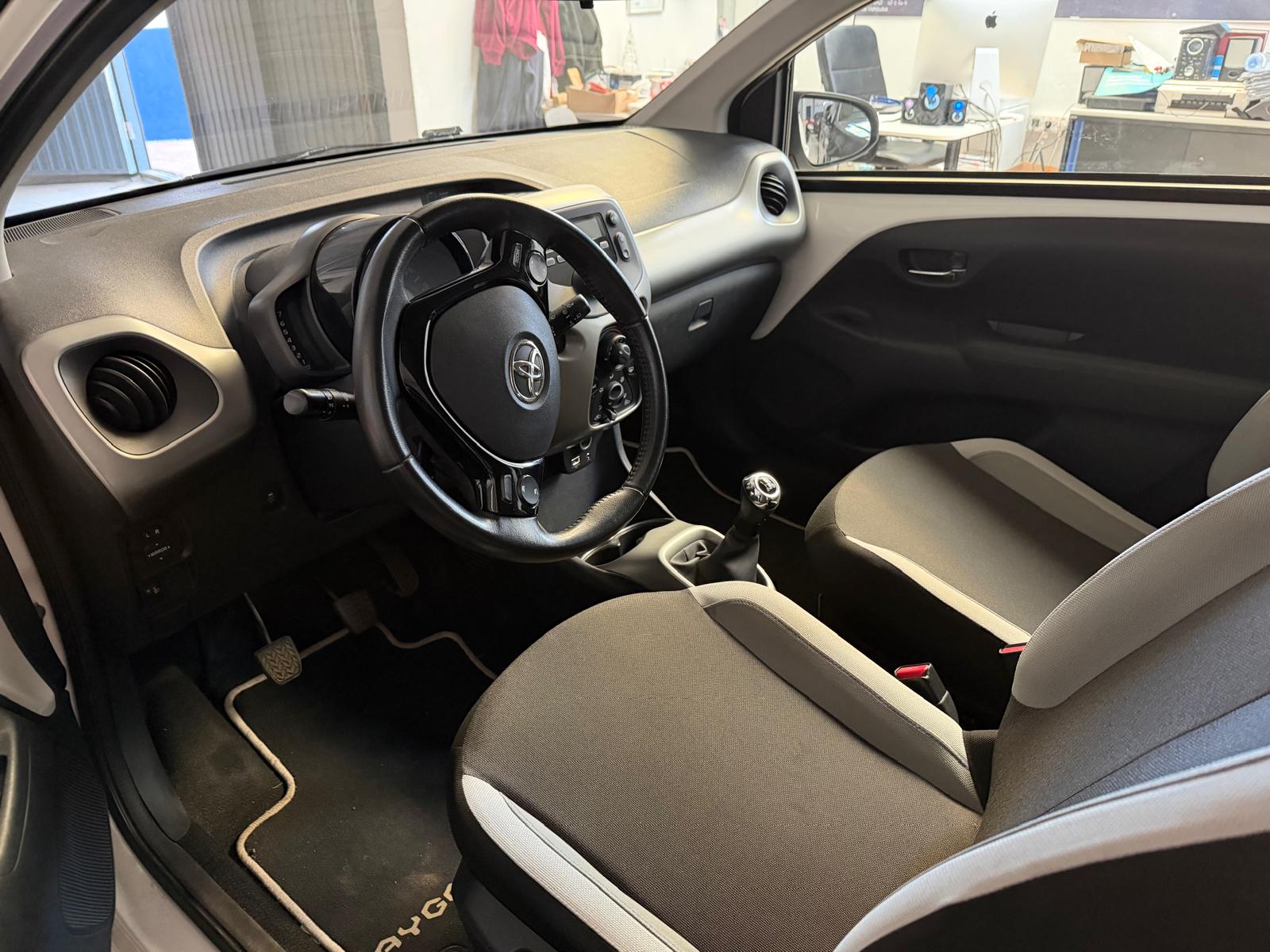 Interior de un automóvil compacto con asientos en tonos gris y negro, volante multifuncional y detalles modernos. Se observa el tablero y la palanca de cambios, destacando un ambiente limpio y bien cuidado. Ideal para reseñas de autos o guías de compra.