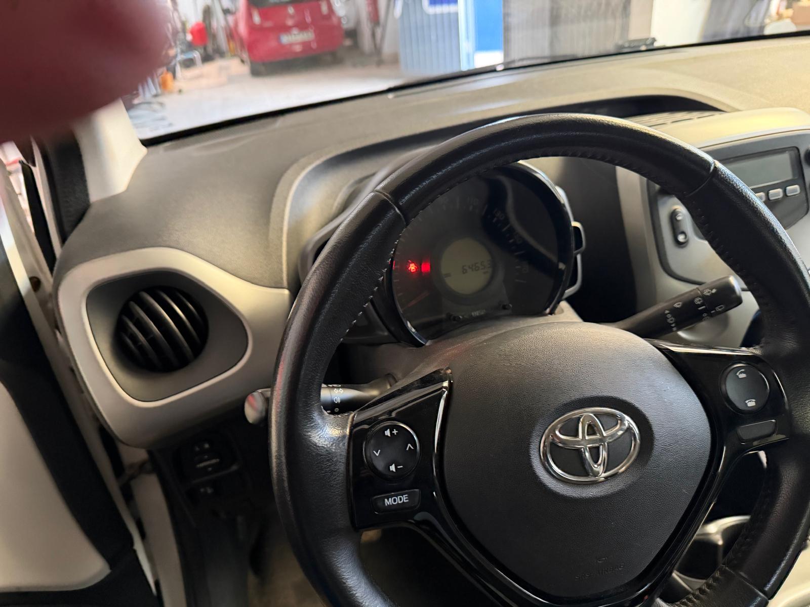 Interior de un automóvil Toyota, mostrando el volante con el logotipo de la marca, el tablero de instrumentos con el odómetro marcando 64653 km y controles de audio. Se observa el diseño moderno del salpicadero y los aireadores.