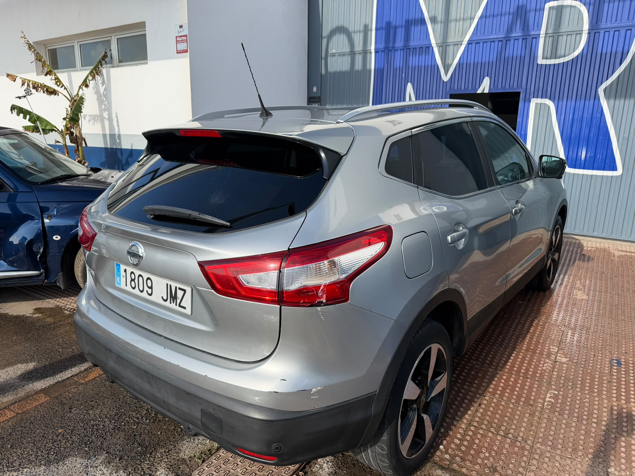 SUV Nissan de color plateado estacionado en un taller, con matrícula I 1809 JMZ, mostrando un diseño moderno y llantas de aleación. Al fondo, se aprecia una pared azul con la letra "MR".