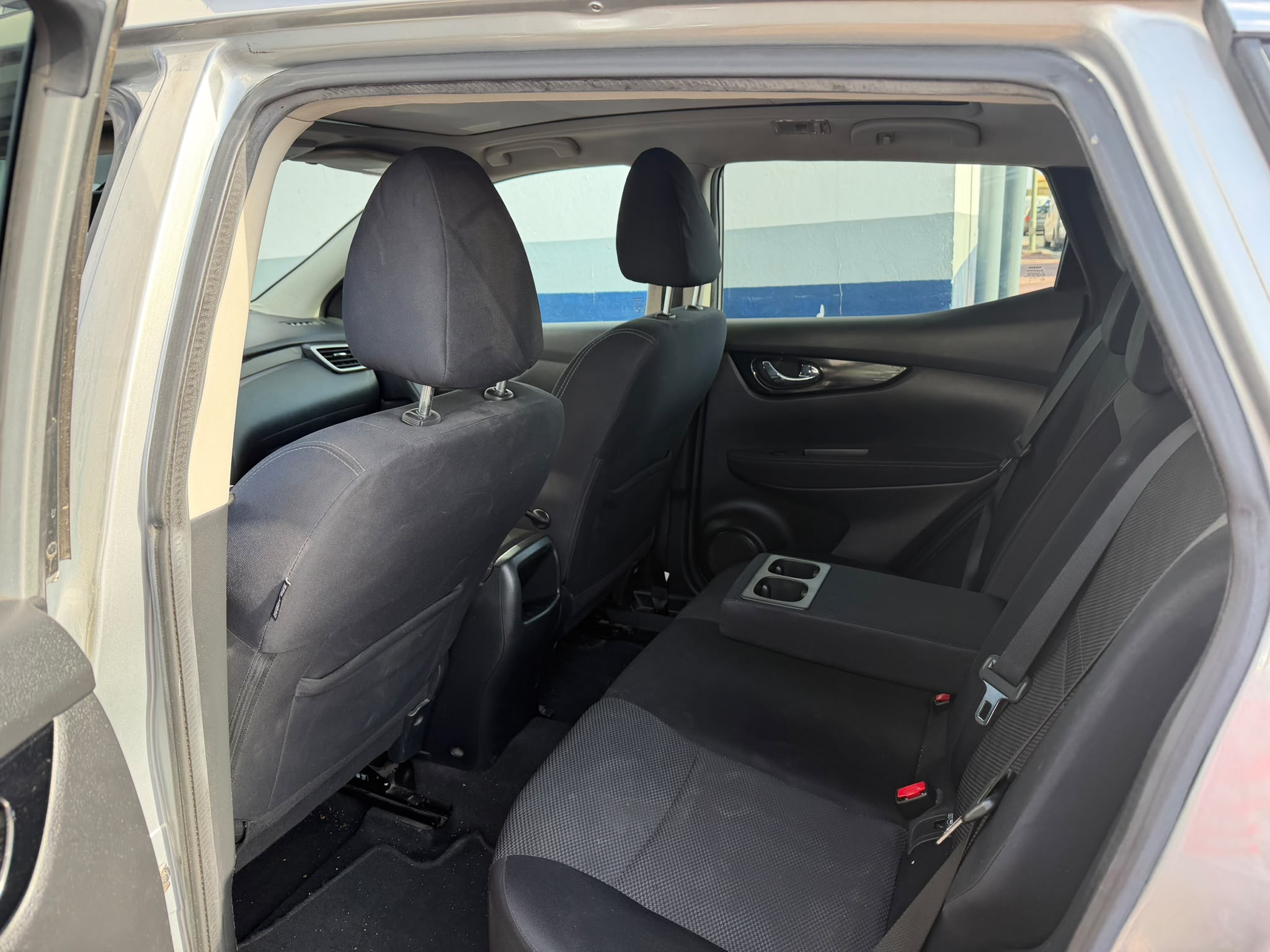 Interior trasero de un automóvil, mostrando asientos cómodos y espacio amplio, ideal para pasajeros. Diseño moderno con detalles en tela oscura y reposabrazos central.
