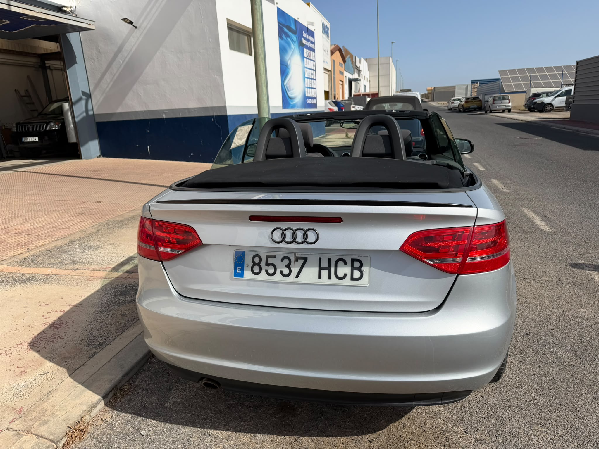 Audi descapotable plateado estacionado en una calle, con el techo abatido y un entorno urbano visible.