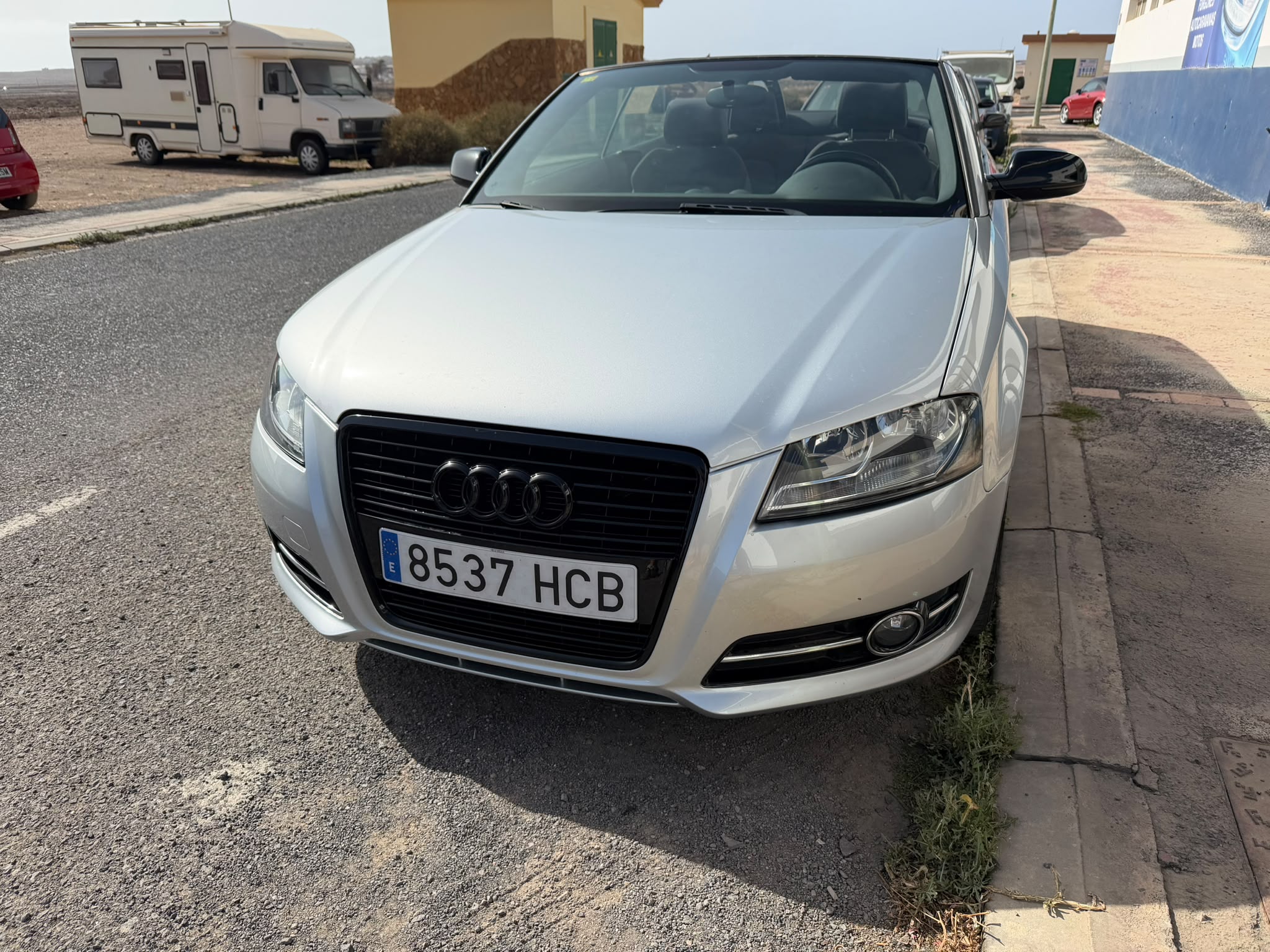 Audi convertible plate 8537 HCB estacionado en la calle, con fondo de vehículos y paisaje desértico.