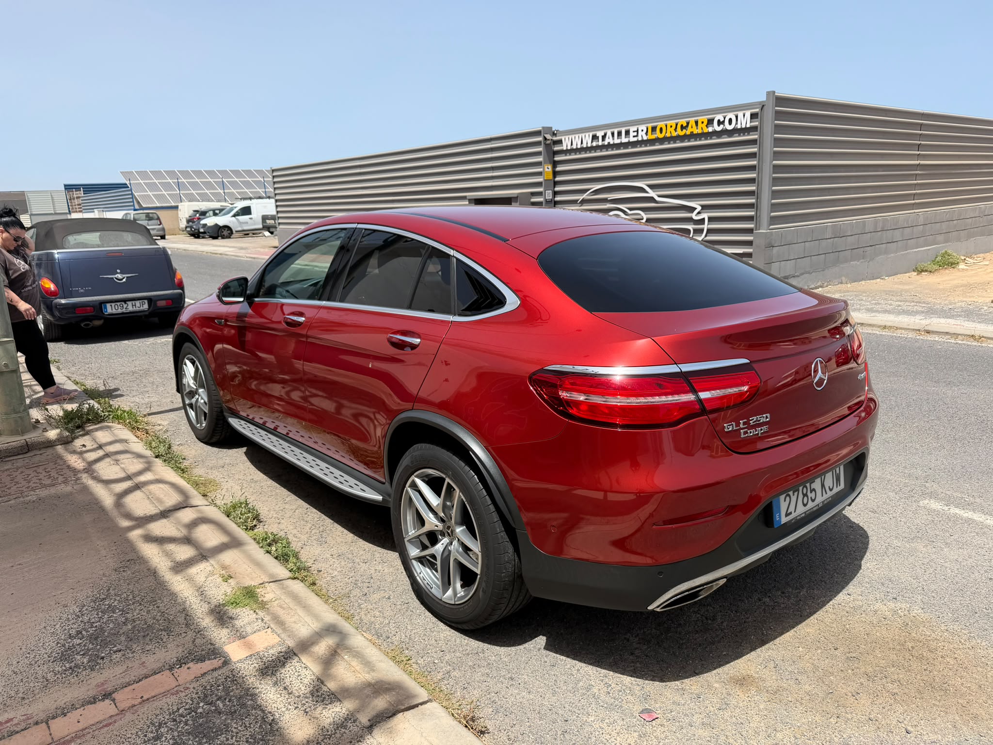 Mercedes-Benz GLE 300 Coupe rojo estacionado en la calle, con un fondo de vehículos y un taller visible.