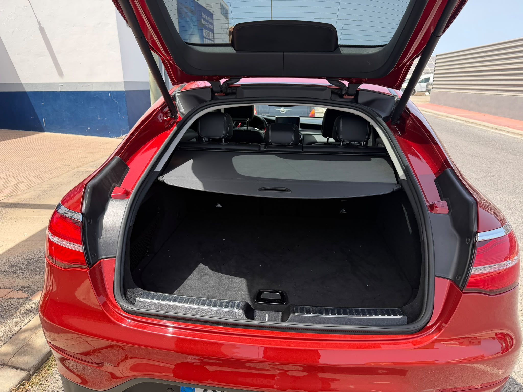 Maletero abierto de un coche rojo, mostrando un espacio amplio y limpio, con un fondo oscuro y una cubierta sobre el área de carga.