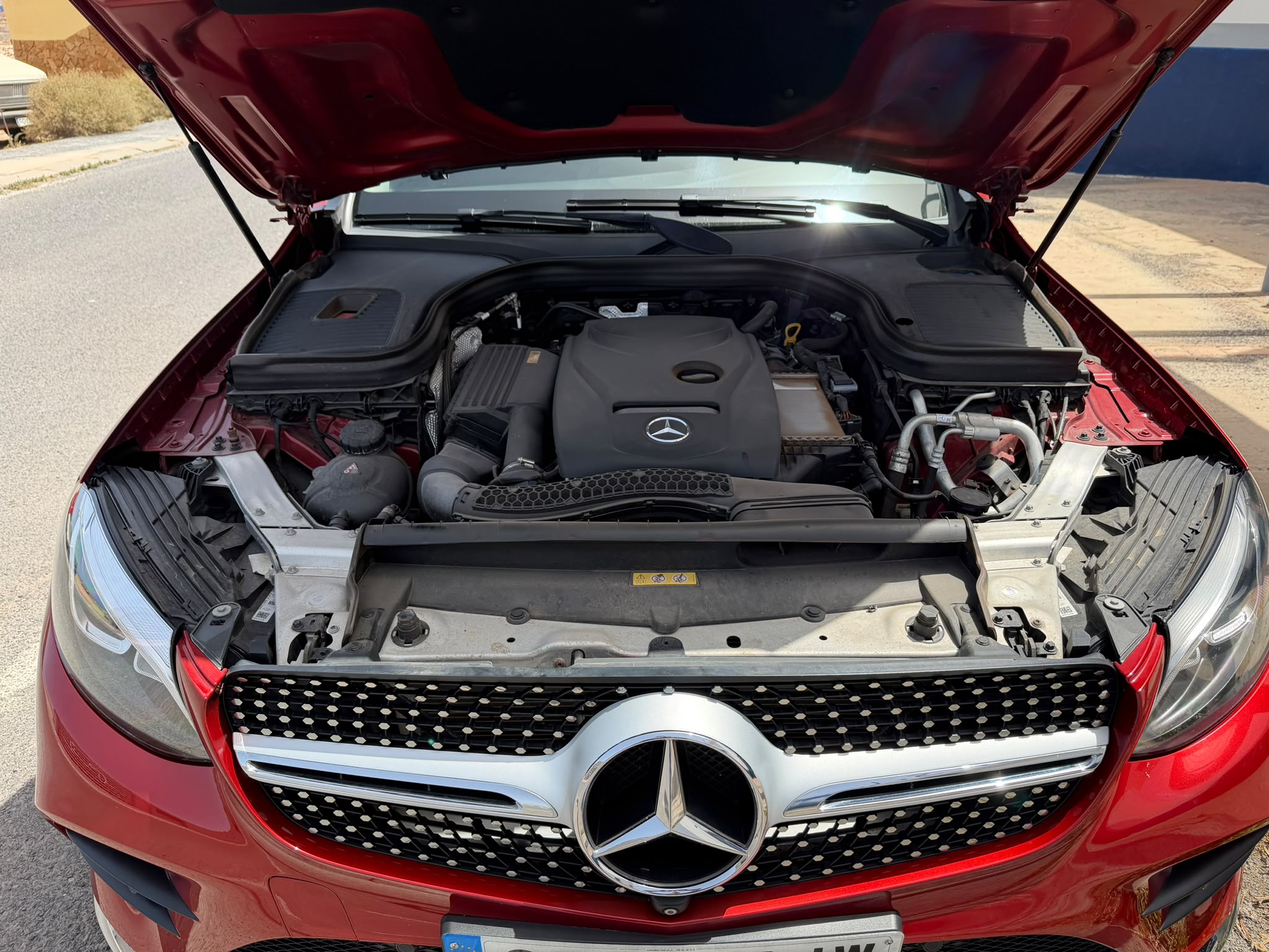 Motor de un automóvil Mercedes-Benz rojo con el capó abierto, mostrando detalles del motor y componentes visibles en el compartimento.