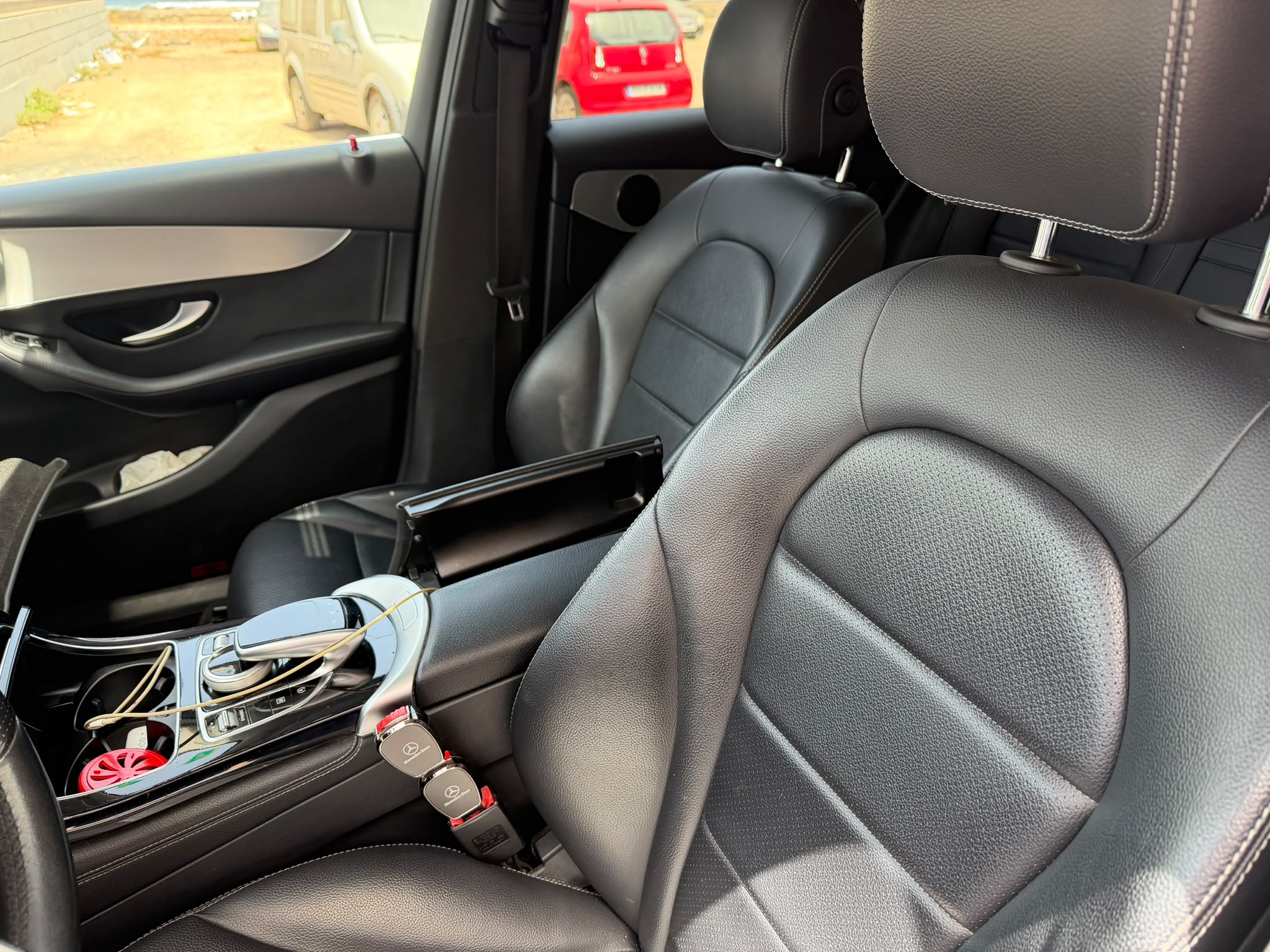 Interior de un automóvil con asientos de cuero negro y consola central, mostrando detalles del diseño moderno y llaves del vehículo. En el fondo se pueden ver otros coches estacionados.