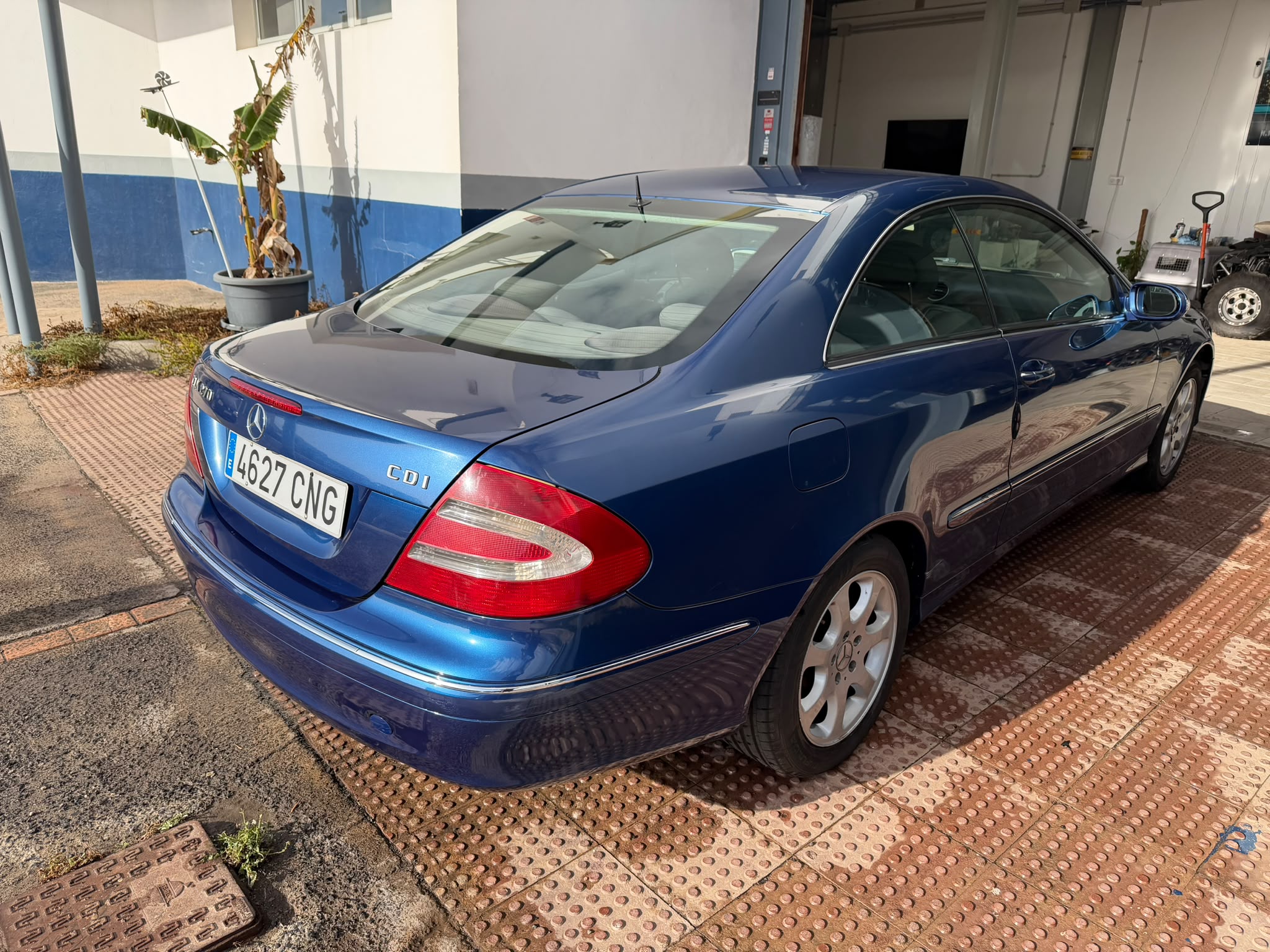 Mercedes-Benz azul estacionado en un área pavimentada, mostrando su diseño elegante y moderno. Se pueden ver detalles como la matrícula 4627 CNG y el logo de la marca en la parte trasera. También hay una planta en una maceta al fondo.