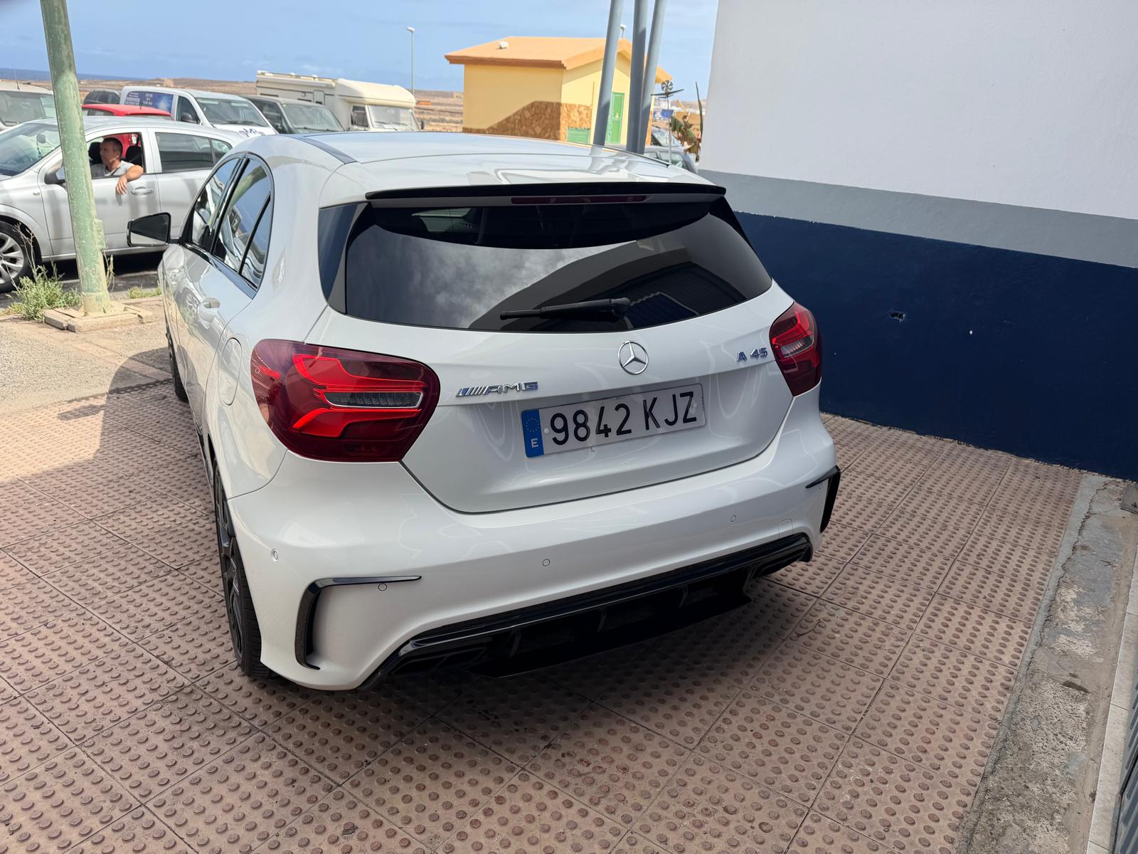 Mercedes-Benz A45 AMG blanco estacionado en una calle, con un diseño deportivo y moderno. Se puede ver el distintivo AMG en la parte trasera, resaltando su potencia y estilo.
