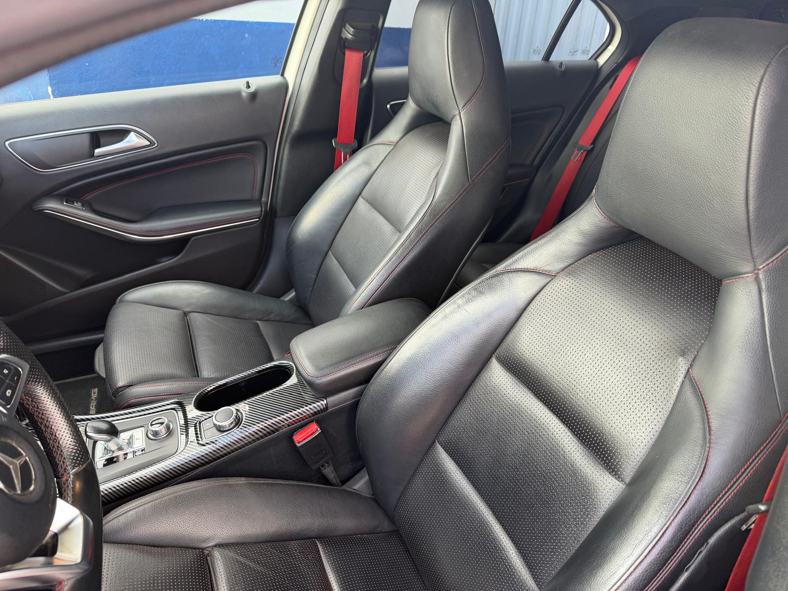Interior de un automóvil Mercedes-Benz con asientos de cuero negro y detalles en rojo, mostrando un diseño moderno y cómodo. Se observa la consola central con controles y acabados de fibra de carbono.